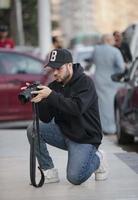 A young man wearing a black hoodie and a black cap photographing in the street photo