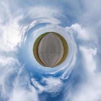 tiny planet in blue overcast sky with beautiful clouds with transformation of spherical panorama 360 degrees. Spherical abstract aerial view. Curvature of space. photo