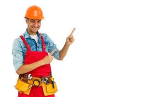 Cheerful male contractor wearing helmet isolated on white background pointing aside while looking at camera photo