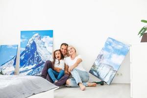 In new flat family hangs a large photo canvas on empty white wall at home