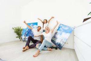In new flat family hangs a large photo canvas on empty white wall at home