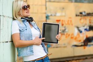 Photo of happy young blonde woman standing over yellow wall background. using tablet computer.