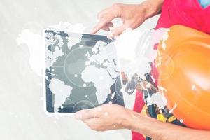 Side view man engineer wearing protective helmet using a tablet computer gadget choosing destinations on the world map. Modern technology artificial intelligence concept photo