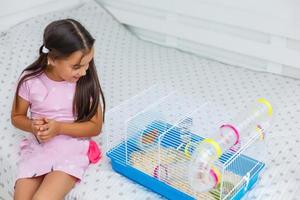 Little girl holds cage for hamster at home photo