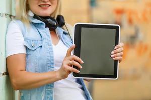 Photo of happy young blonde woman standing over yellow wall background. using tablet computer.