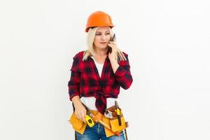 Retrato de una joven ingeniera sonriente con casco de seguridad amarillo de pie con espacio de copia de teléfono móvil aislado en un estudio de fondo blanco foto