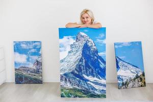 Happy blonde woman hanging large picture on wall at home photo