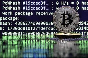 Two bitcoins lies on a videocard surface with background of screen display of cryptocurrency mining by using the GPUs photo