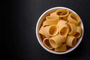 Raw uncooked pasta in a white ceramic bowl with spices and herbs photo