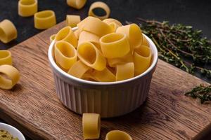 Raw uncooked pasta in a white ceramic bowl with spices and herbs photo