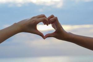 Sunlight shines through hands interlaced in heart shape on evening sky background. soft and selective focus. photo