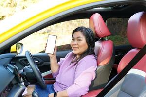 Asian woman sitting in a yellow car and one hand shows a mobile phone concept travel, driving, navigation, travel, leisure. Soft and selective focus. photo