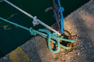 anillo de amarre con cuerda náutica azul y blanca atada montada en un muelle de hormigón, equipo de seguridad marina foto