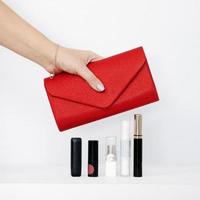 Female hand holding a red purse above five packages of lipstick photo