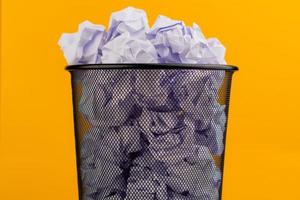 trozos blancos de papel en el bote de basura sobre un fondo amarillo, concepto de desperdicio de papel usado foto