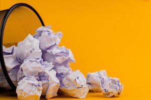 trozos blancos de papel en el bote de basura sobre un fondo amarillo, concepto de desperdicio de papel usado foto