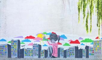 The old wall, painted in color graffiti drawing with aerosol paints. Picture of a little girl who draws a lot of skyscrapers with a brush with paints photo