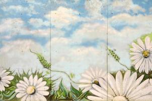 Background texture of wall with graffiti paintings. Blue cloudy sky and white flowers photo