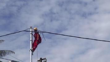 Gorontalo-Indonesia, December 2022 - Technicians connect cables to electric poles. Employee hanging by belt on electricity pole for laying low voltage cable video