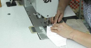 A Seamstress Sewing The Strip Of Elastic Garter Making Ear Loops On A White Face Mask In A Sew Factory - Covid-19 Pandemic - Medium Shot Pan Right video