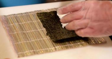 Chef Puts Seaweed Wrap And Sushi Rice On A Bamboo Mat For Rolling - close up, slow motion video