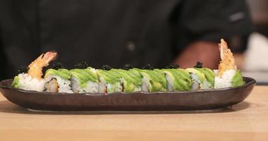 chef poniendo caviar de sushi negro de hueva encima de rollo de sushi de tempura de camarones con rodajas de aguacate usando una cucharadita - primer plano, tiro panorámico video