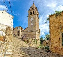 View over the cobblestone historic access road to Motovun with evangelical church during the day photo