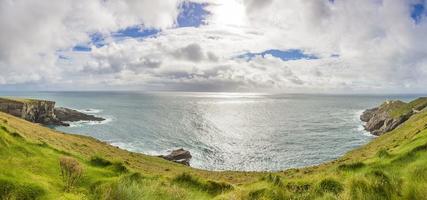 Panorama picture of typical Irish coast line with green meadows and blue waters during daytime photo