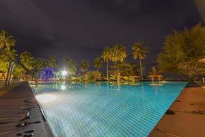 Impression from illuminated swimming pool at night in tropical garden with palm trees photo