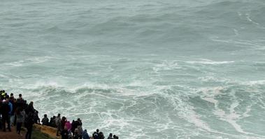 eine riesige menschenmenge beobachtet die mächtigen wellen von nazare, portugal - wellenbeobachtung - zeitlupe video