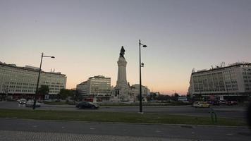 vehículos de transporte en la concurrida carretera en la plaza marques de pombal en lisboa, portugal durante la puesta de sol con la estatua de bronce del marqués en el centro de la rotonda - lapso de tiempo