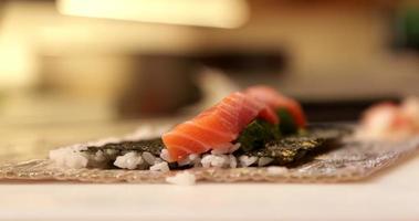 capocuoco nel il cucina fabbricazione un' Sushi rotoli - fresco salmone filetto in cima su nemmeno io alghe e giapponese riso al di sopra di bambù stuoia. - vicino su tiro video