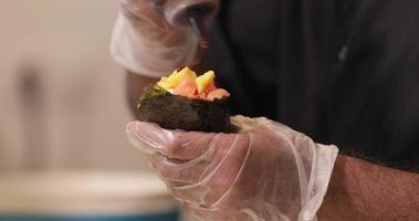 chef con guantes sosteniendo un cono de sushi o un rollo de mano y poniendo salsa y cebolla antes de servir. - fotografía de cerca video