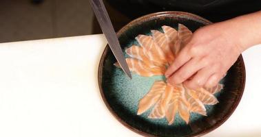 pose de fines tranches de filet de saumon non cuit dans une assiette ronde à l'aide d'un couteau de cuisine - prise de vue panoramique video