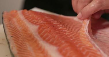 een chef trimmen de vlees van een vers Zalm filet gebruik makend van een scherp mes voor sushi. - dichtbij omhoog schot video