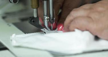 aguja de máquina de coser utilizada por una costurera para coser máscaras de tela blanca en una industria de la confección - primer plano extremo video