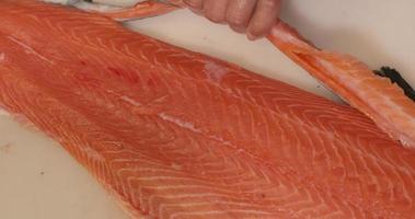chef cortando y quitando aletas de filete de salmón fresco en la tabla de cortar de la cocina. fileteado de salmón para sushi. - fotografía de cerca video