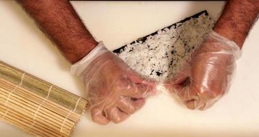Hände verteilen Sushi-Reis auf Seetang-Wrap - Aufnahme von oben, Zeitlupe