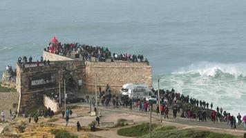 die menschen genießen es, intensive wellen auf dem leuchtturm von nazare in portugal zu beobachten - zeitlupenaufnahme video