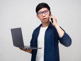Asian businessman holding laptop with talking mobile busy and serious isolated photo
