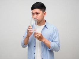 joven asiático sostiene un vaso de agua y gesticula con olor aislado foto
