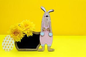 Wooden rabbit with black board for text and chrysanthemums, an egg on yellow background. Easter concept. Copy space photo