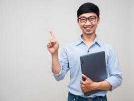 Young businessman gentle smile holding laptop point finger isolated photo