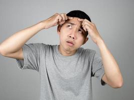hombre asiático camisa gris se siente preocupado por el acné de su cara aislado foto