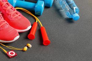 Top view of sports equipment, dumbbells, a skipping rope, a bottle of water, sneakers and a player. Isolated on a gray photo
