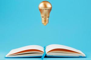 A gold-colored light bulb hangs above the blank pages of a notebook on a blue background. photo