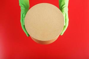 The parcel from the delivery service in the hands with green rubber gloves on a red background. photo