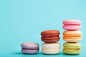 Macaroni cookies of different colors are arranged in the shape of pyramid steps on a blue background. photo