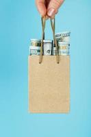 A small aid Bag made of paper in an outstretched hand with US dollars on a blue background. Packaging template layout with space for copying, advertising. photo