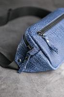 Waist bag made of blue leather, banana on a gray background. photo